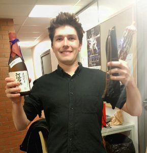 Julien arborant fièrement une bouteille de breuvage japonais et un saucisson réparateur